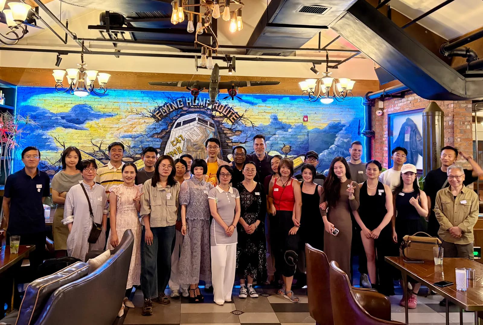 A large group in front of the Flying Hump Route mural, the C-47 model hanging overhead