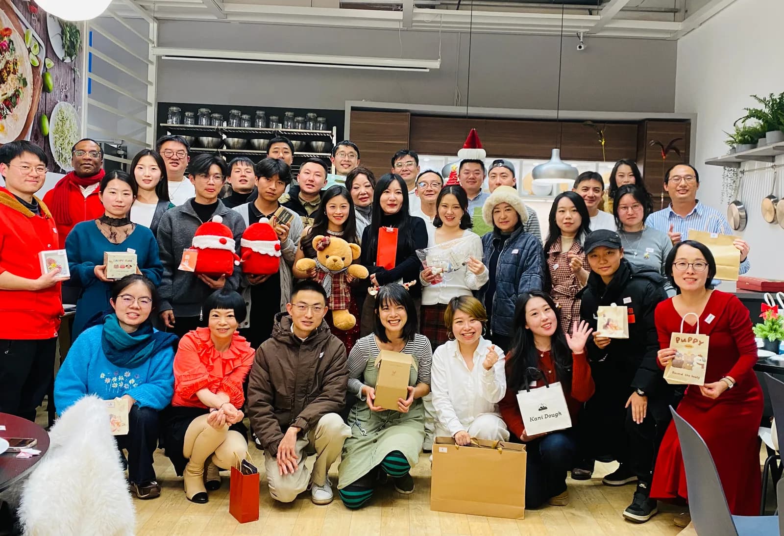 A big group photo at the Christmas meet-up, everyone holding the gift they swapped