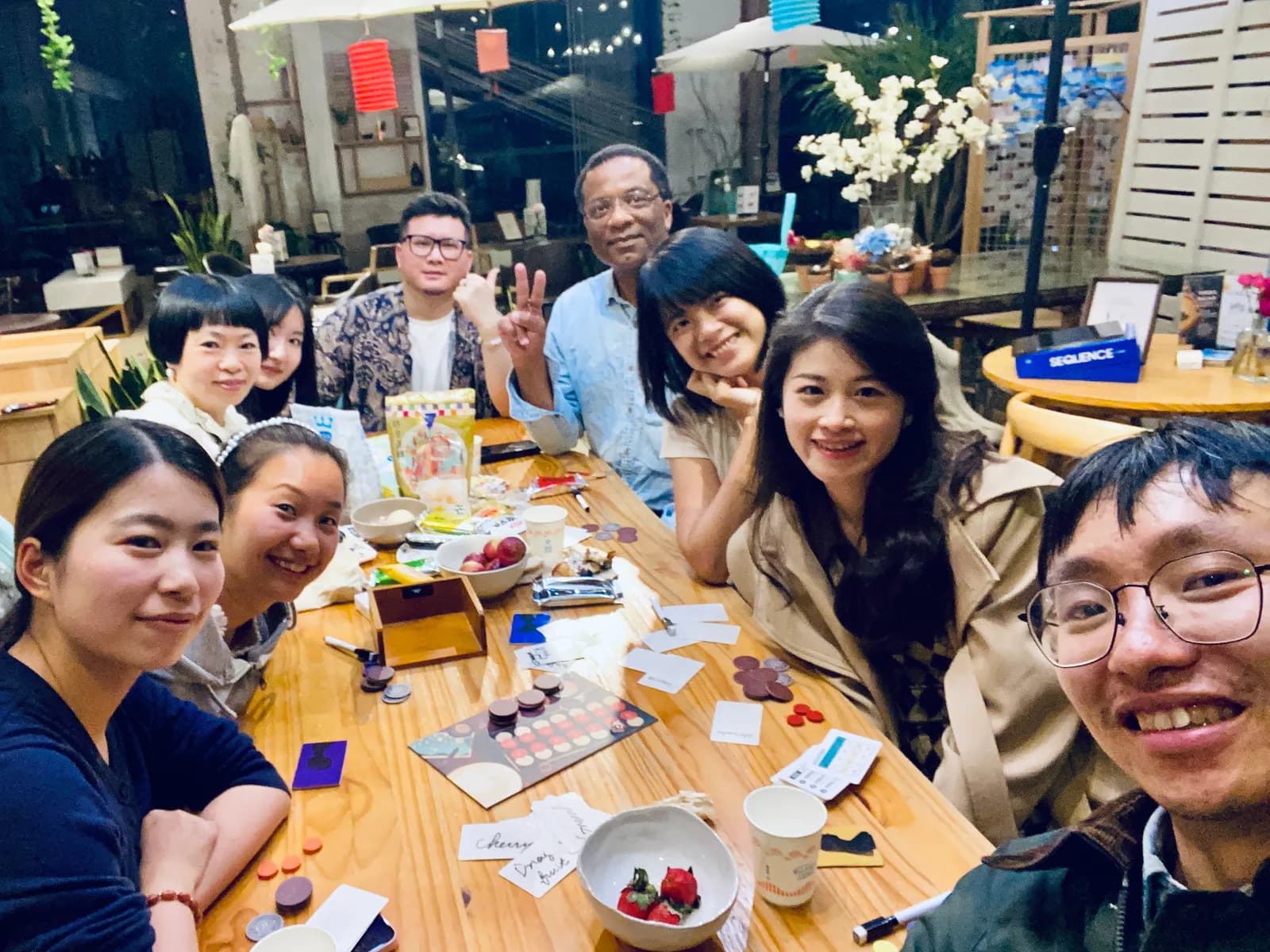 A selfie of nine players around a table covered in cards, tokens and snacks