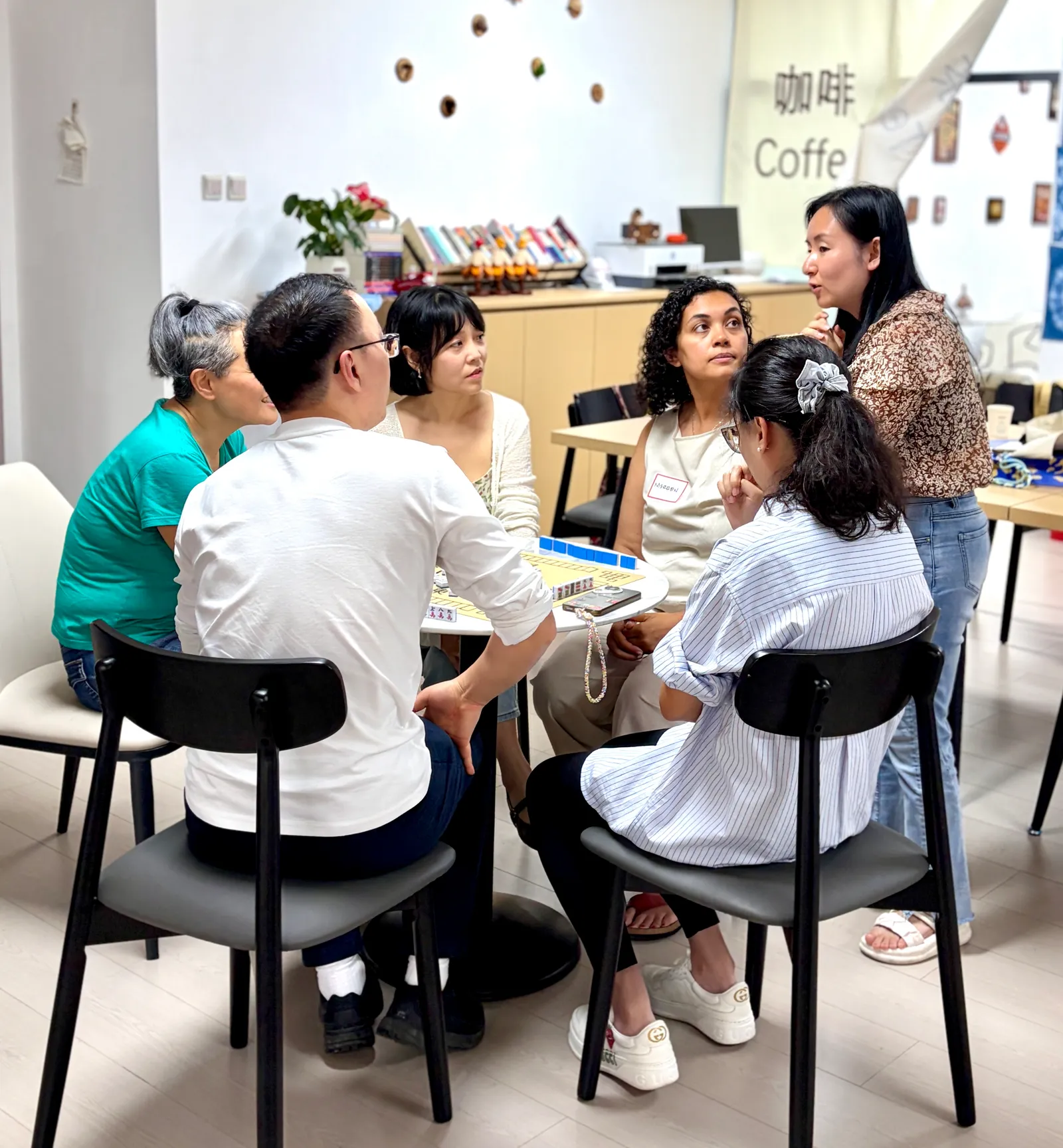 A mahjong table in full swing, with others leaning in to follow the hands